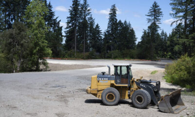 Yellow Deere wheel loader with a large front bucket on a gravel construction site, trees in the background.