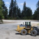 Yellow Deere wheel loader with a large front bucket on a gravel construction site, trees in the background.