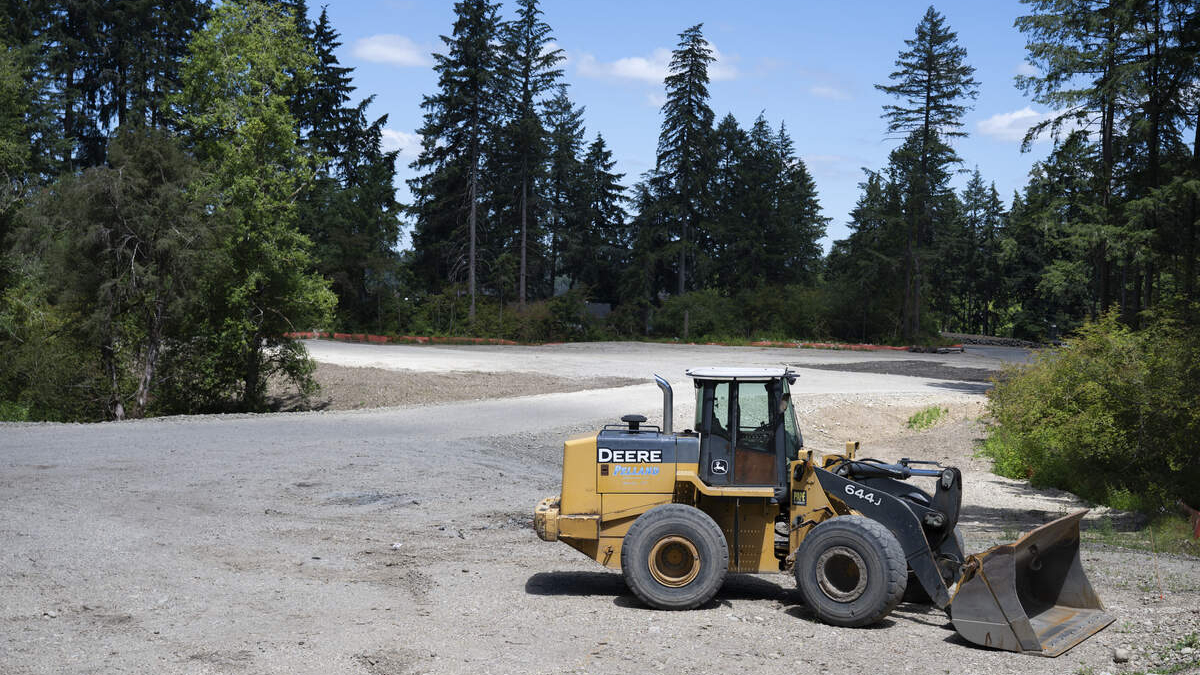 Yellow Deere wheel loader with a large front bucket on a gravel construction site, trees in the background.
