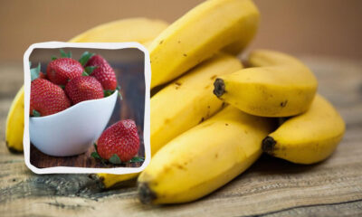 Bananas on a wooden surface with an inset frame showing a white bowl of strawberries.