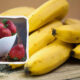 Bananas on a wooden surface with an inset frame showing a white bowl of strawberries.