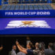 Cameras and reporters photograph a blue FIFA World Cup 2026 entrance canopy with the event logo.