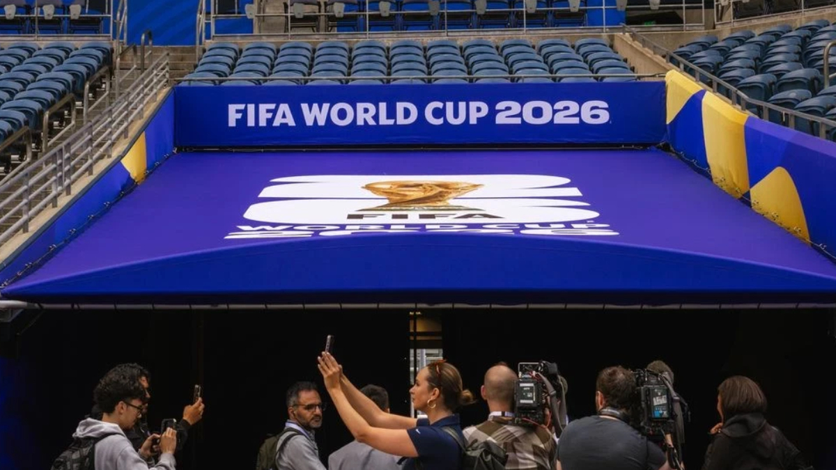 Cameras and reporters photograph a blue FIFA World Cup 2026 entrance canopy with the event logo.