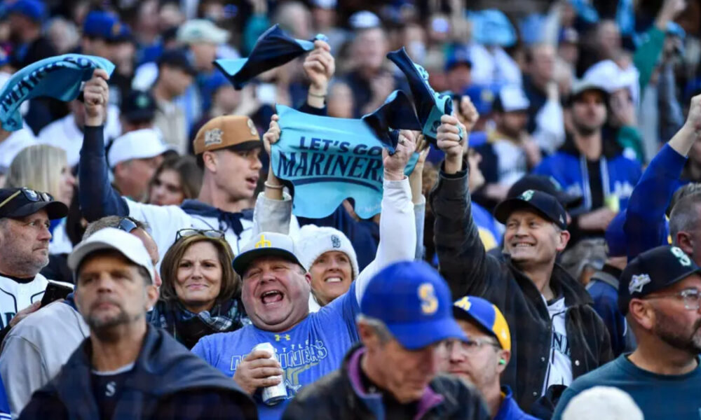 Crowd of Seattle Mariners fans cheering in a stadium, waving blue towels and banners.