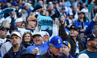 Crowd of Seattle Mariners fans cheering in a stadium, waving blue towels and banners.