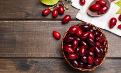 Basket filled with red cherries on a dark wooden table; a few loose cherries nearby.