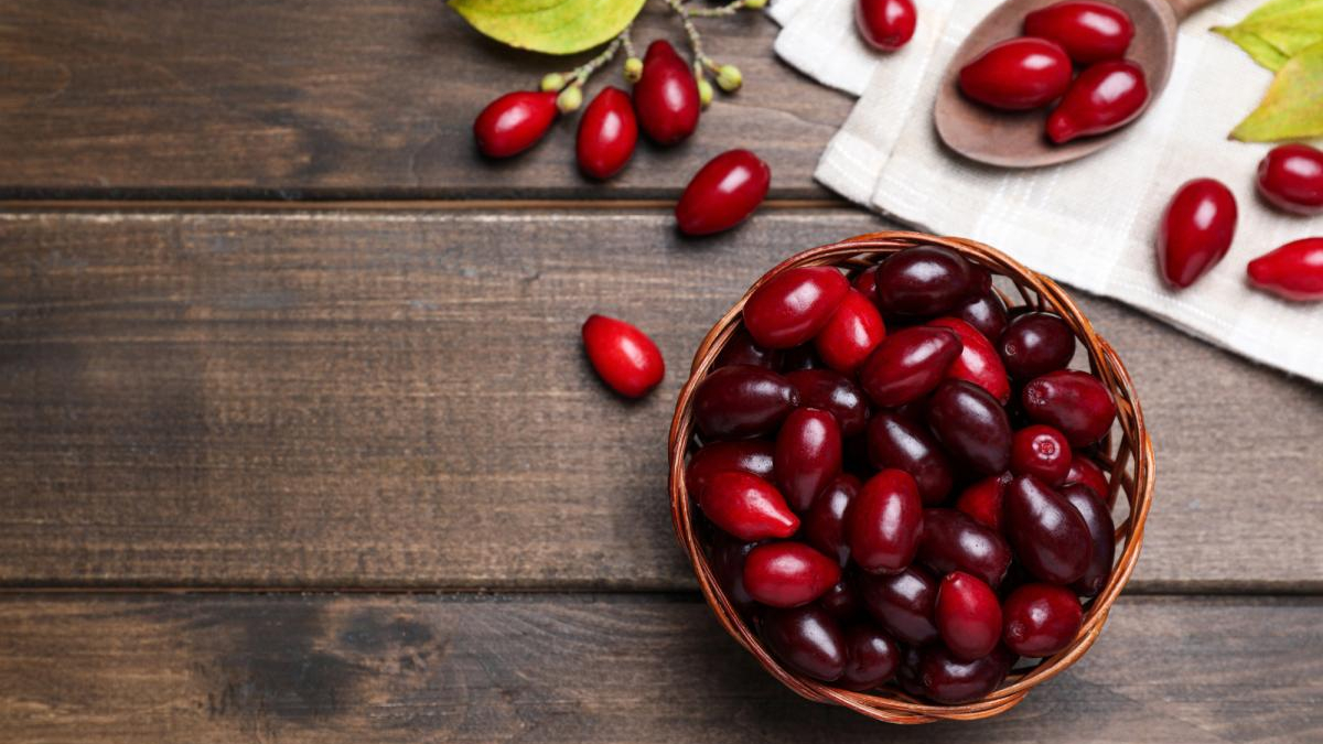 Basket filled with red cherries on a dark wooden table; a few loose cherries nearby.