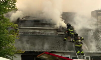 Firefighters on a smoke-filled roof spraying water to extinguish a residential fire.