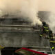 Firefighters on a smoke-filled roof spraying water to extinguish a residential fire.