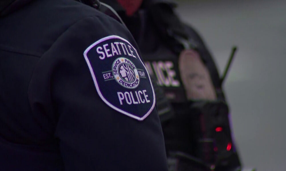 Close-up of a Seattle Police patch on a dark uniform, showing the circular emblem in the center of the sleeve