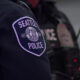 Close-up of a Seattle Police patch on a dark uniform, showing the circular emblem in the center of the sleeve