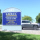 Large blue Kadlec clinic sign with 945 address, surrounded by greenery; a silver SUV is parked to the right on a sunny day.