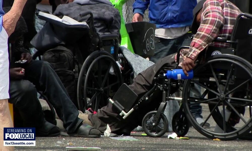 Group of people in wheelchairs gathered on a street with litter, a news logo visible in the corner (FOX Local).