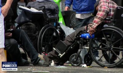 Group of people in wheelchairs gathered on a street with litter, a news logo visible in the corner (FOX Local).
