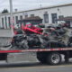 Tow truck carrying a severely wrecked gray sports car on a flatbed in an industrial lot