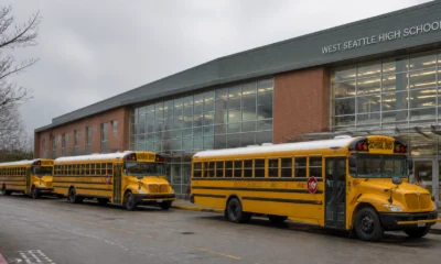 Three yellow school buses parked in front of West Seattle High School with a glass-front entrance and brick facade.