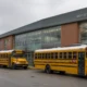 Three yellow school buses parked in front of West Seattle High School with a glass-front entrance and brick facade.
