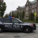 Seattle Police SUV with red and blue lights parked on a tree-lined city street in front of brick, campus-style buildings.