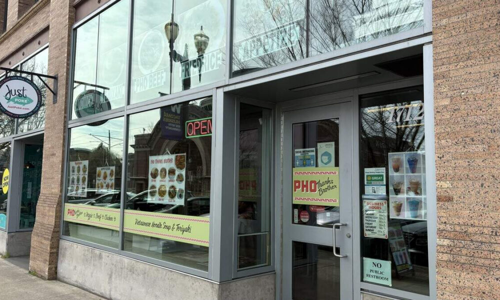 Exterior of a Vietnamese restaurant with large glass windows, menu posters, and a lit OPEN sign outside a brick building.