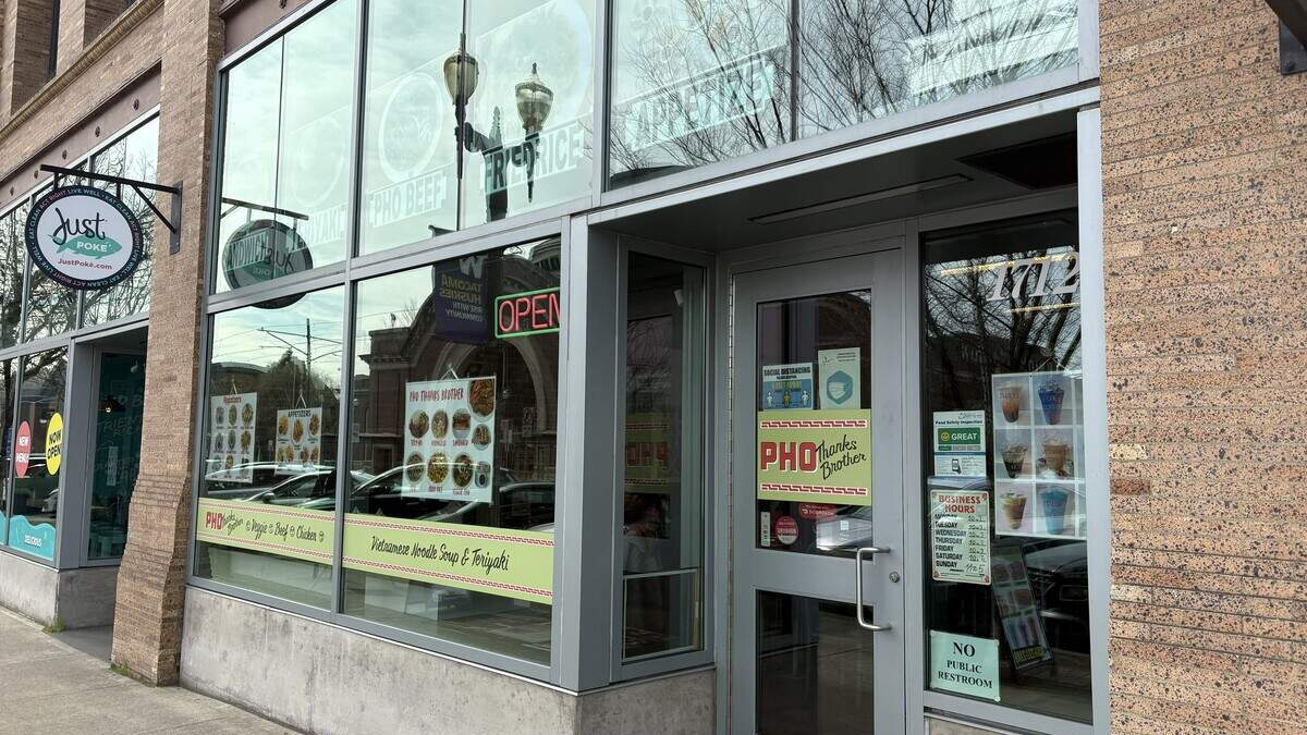 Exterior of a Vietnamese restaurant with large glass windows, menu posters, and a lit OPEN sign outside a brick building.