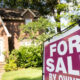 A large magenta 'FOR SALE' sign in the yard with a brick suburban house and greenery in the background.