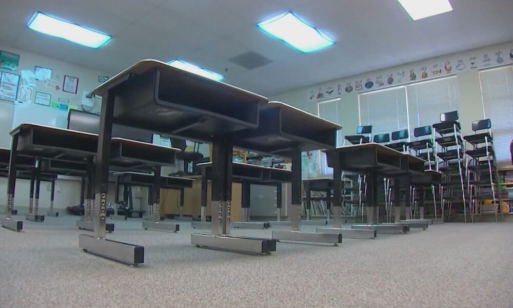 Low-angle view of an empty classroom with rows of desks and stacked chairs along the back wall.