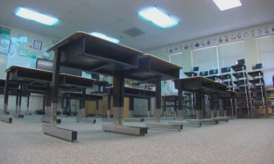 Low-angle view of an empty classroom with rows of desks and stacked chairs along the back wall.