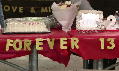 Table covered in red cloth with gold glitter letters spelling 'FOREVER 13', a wedding-style cake under a plastic cover, bouquet, decorative framed photo, and a lit decorative '2' at a celebration setup.