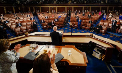Congressional chamber: a leader stands at the central podium addressing seated lawmakers wearing masks in a semicircular chamber.