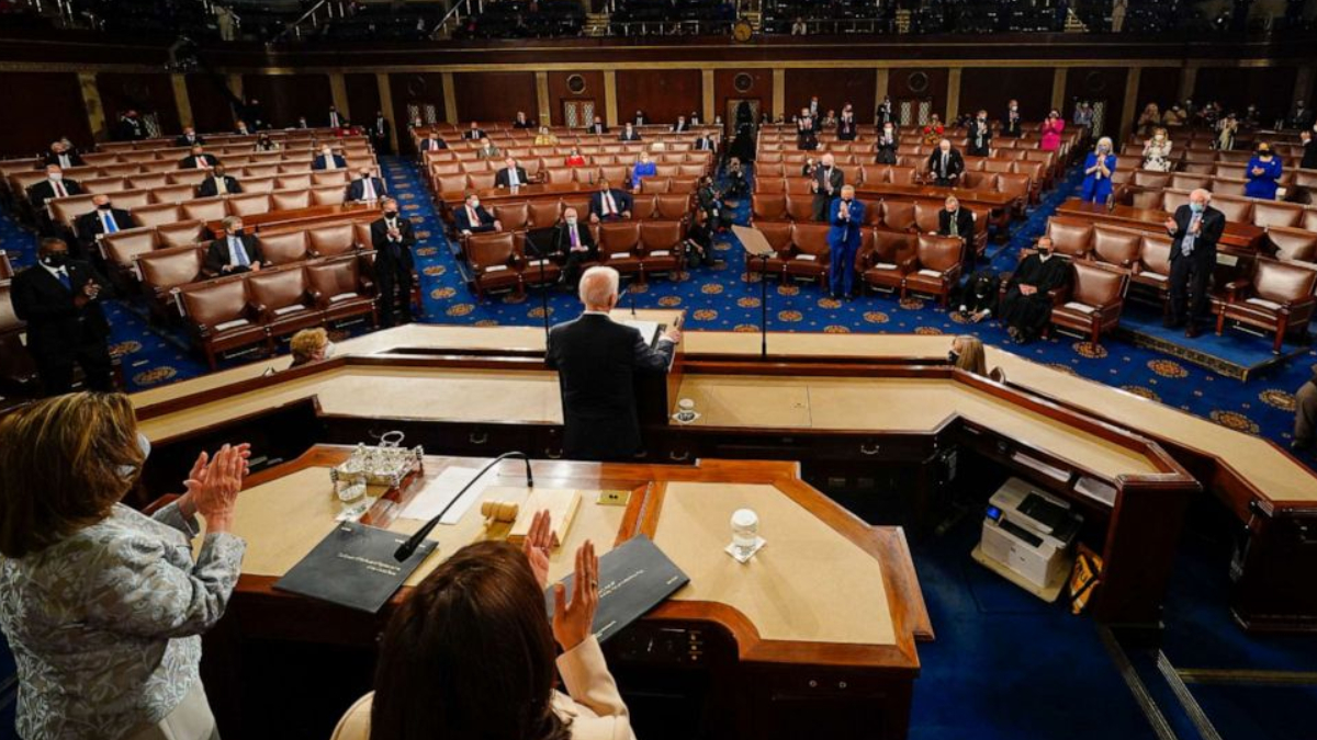 Congressional chamber: a leader stands at the central podium addressing seated lawmakers wearing masks in a semicircular chamber.