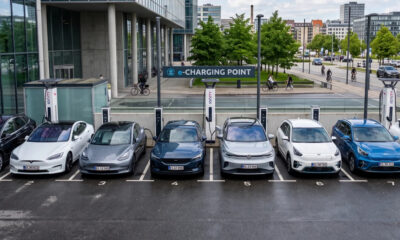 Row of electric cars parked at individual charging bays in front of a modern building at an e-charging point