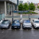 Row of electric cars parked at individual charging bays in front of a modern building at an e-charging point