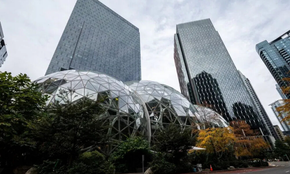 Geodesic glass domes in a modern city plaza surrounded by tall glass skyscrapers and trees.