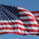 American flag waving on a flagpole against a clear blue sky.