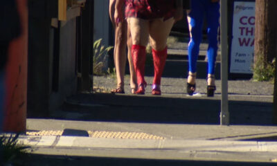 People walking away on a sidewalk, seen from behind; one person wears bright red knee-high socks and heels, others in sandals or flats nearby.
