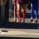 People walking away on a sidewalk, seen from behind; one person wears bright red knee-high socks and heels, others in sandals or flats nearby.