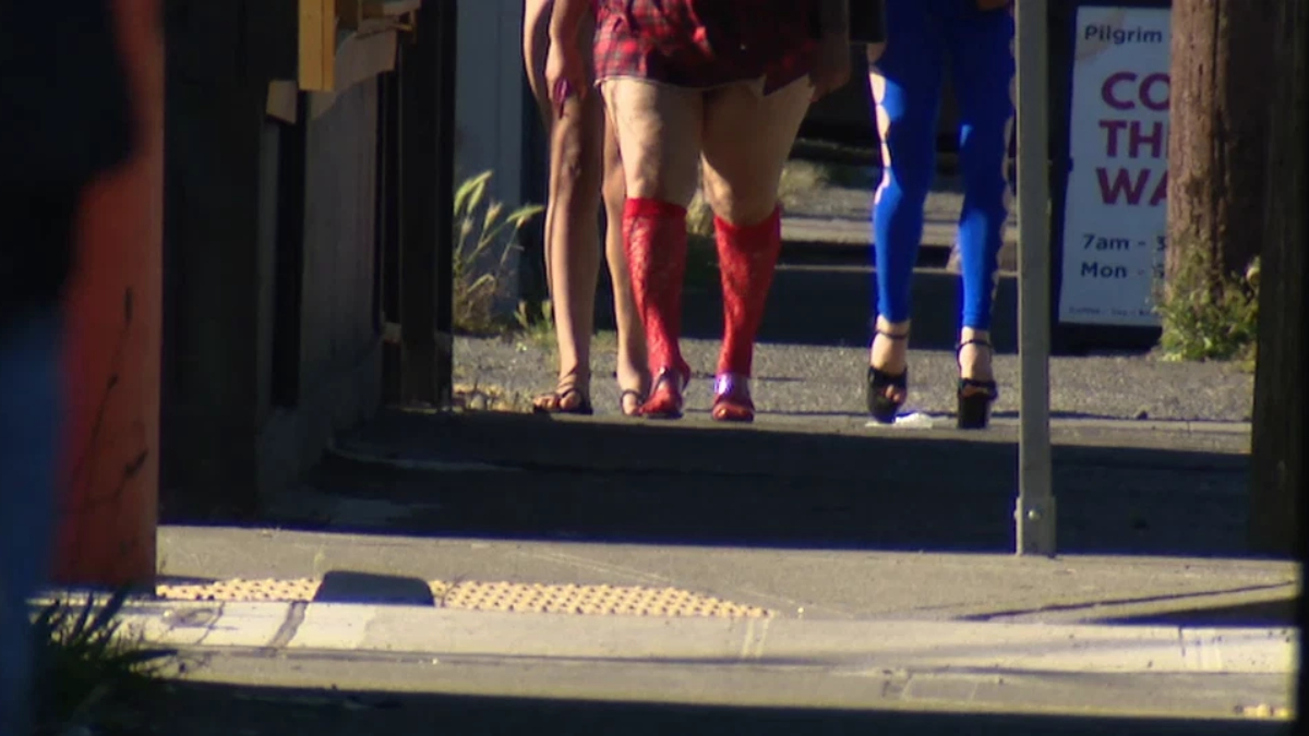 People walking away on a sidewalk, seen from behind; one person wears bright red knee-high socks and heels, others in sandals or flats nearby.