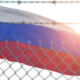 Russian flag waving behind a chain-link fence with barbed wire, sun flare in the background