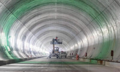 Inside a large cylindrical tunnel under construction, a scissor lift with a worker elevated near equipment.