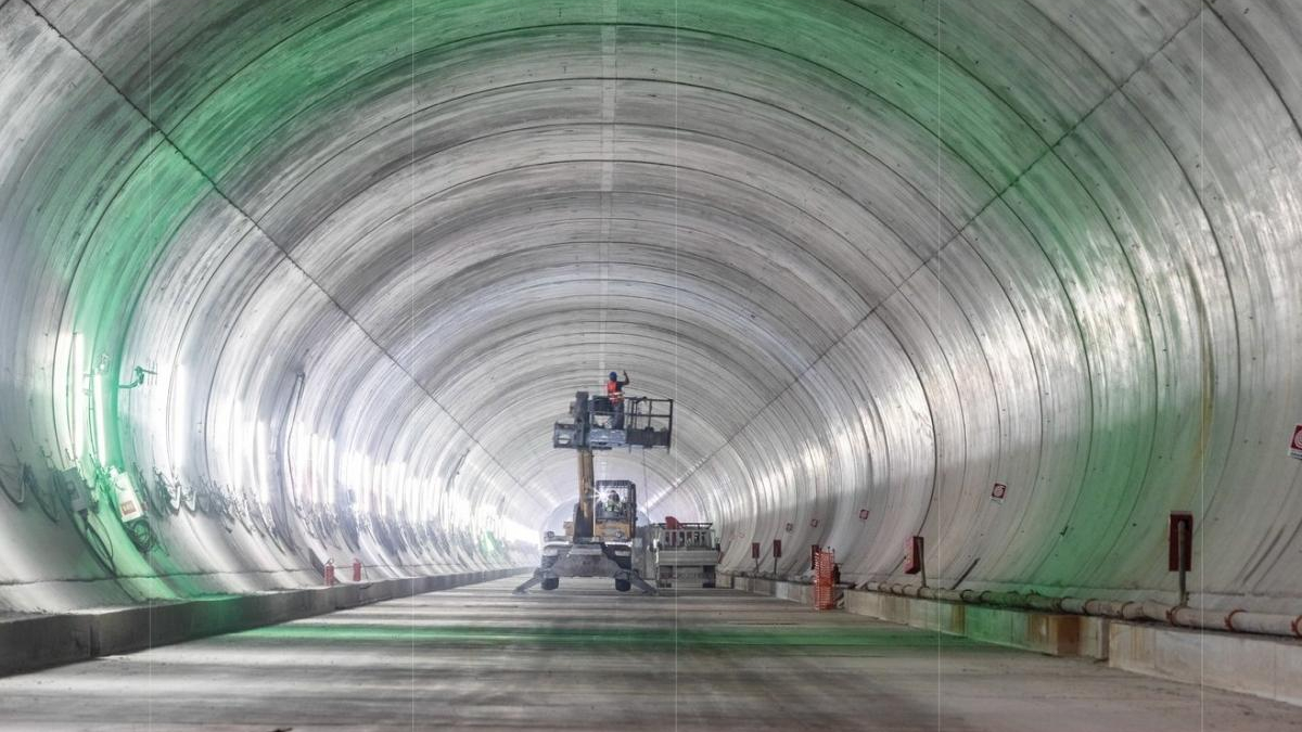 Inside a large cylindrical tunnel under construction, a scissor lift with a worker elevated near equipment.