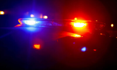 Police car with red and blue emergency lights flashing at night, horizon darkened with blurred city lights in the background