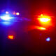 Police car with red and blue emergency lights flashing at night, horizon darkened with blurred city lights in the background