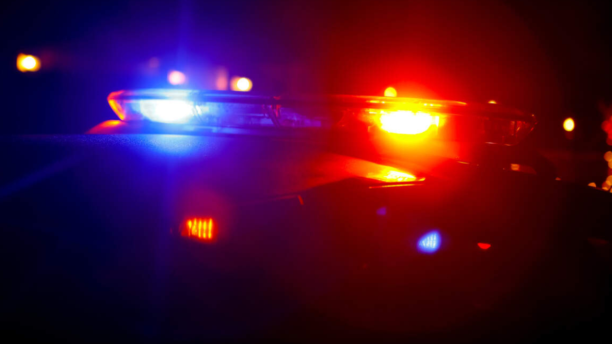 Police car with red and blue emergency lights flashing at night, horizon darkened with blurred city lights in the background