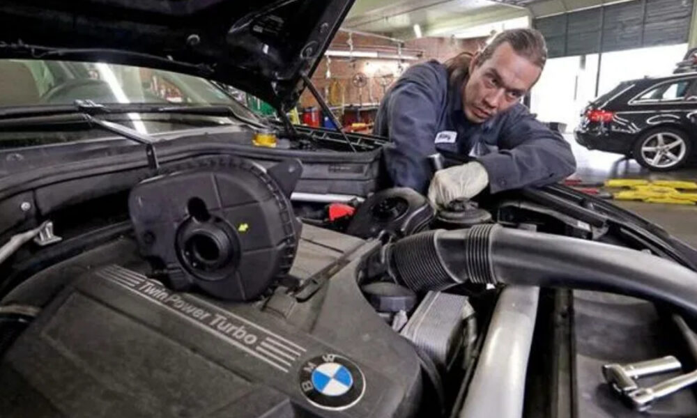 Mechanic leaning over open BMW hood, inspecting the engine in a workshop