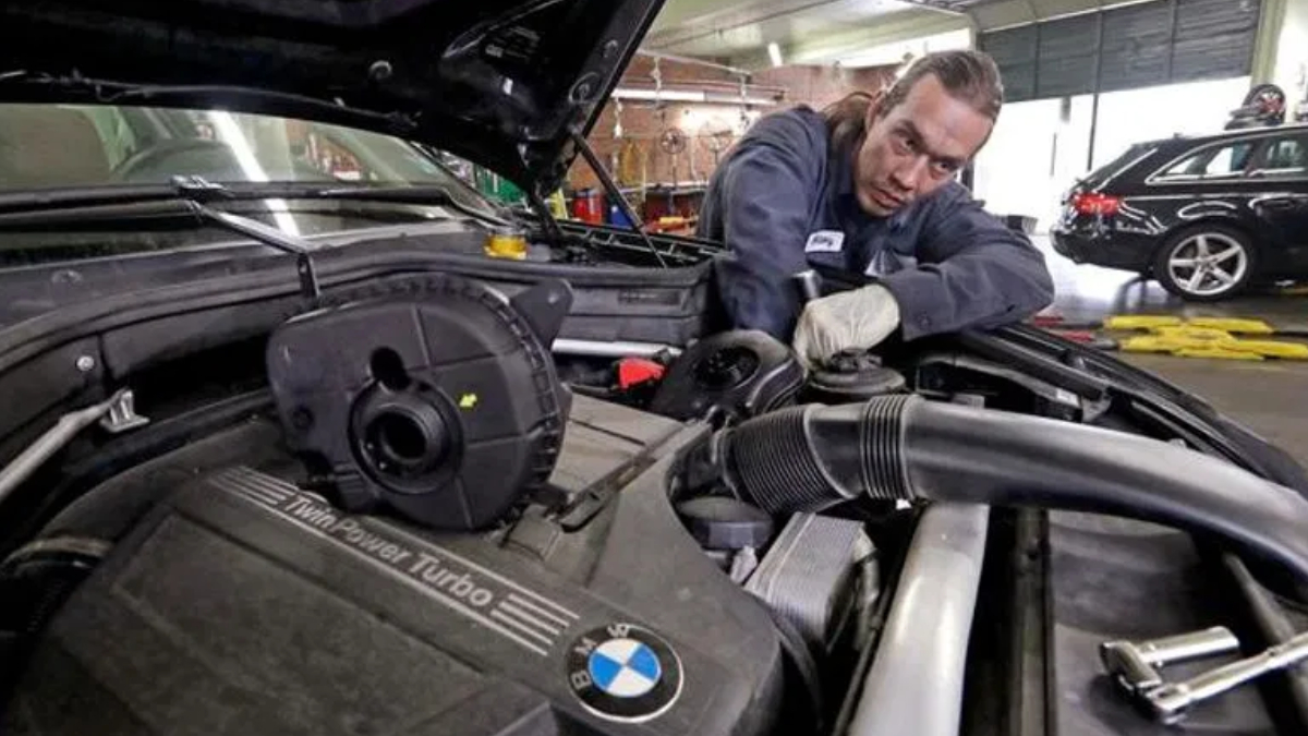 Mechanic leaning over open BMW hood, inspecting the engine in a workshop