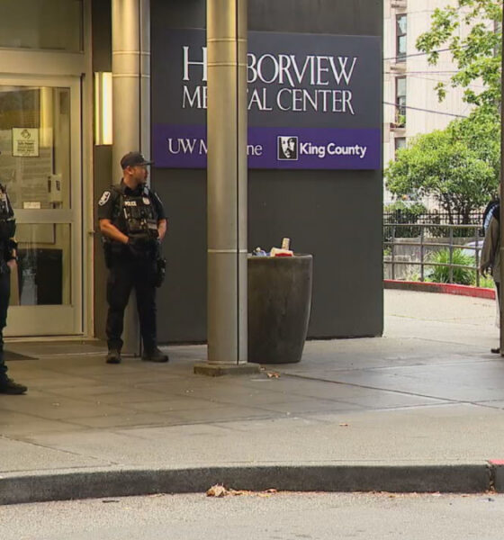 Four police officers in tactical gear stand guard outside Harborview Medical Center entrance and signage visible above.