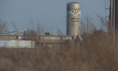 Tall silo with Moses Lake branding behind low industrial buildings, with dry brush in the foreground.