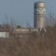 Tall silo with Moses Lake branding behind low industrial buildings, with dry brush in the foreground.
