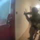 A group of soldiers in tactical gear with rifles advancing down a hallway toward a doorway, ready for entry.