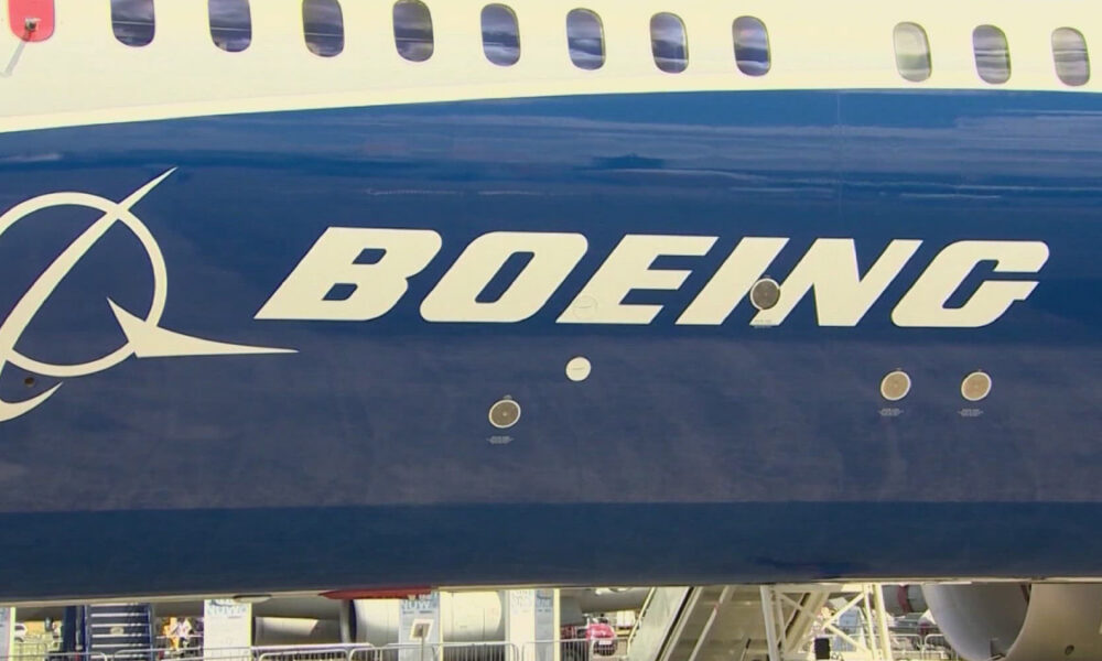 Close-up of a Boeing airplane fuselage featuring the white BOEING logo on a dark blue body with passenger windows above.